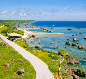 Küstenstraße auf Okinawa mit Blick auf das türkisblaue Meer, gesäumt von grünen Wiesen und verstreuten Felsen im Wasser.