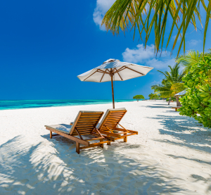 Zwei Liegestühle mit Sonnenschirm an einem weißen Sandstrand in Sri Lanka, umgeben von Palmen und türkisfarbenem Meer.