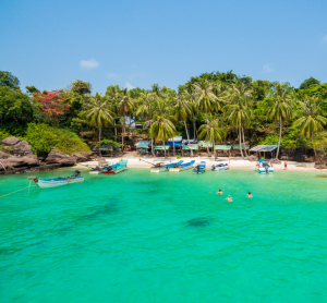 Klares türkisfarbenes Wasser mit kleinen Booten und Palmenstrand in Südvietnam.