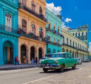 Klassischer Oldtimer fährt an bunten Kolonialgebäuden in Havanna, Kuba, bei blauem Himmel vorbei.