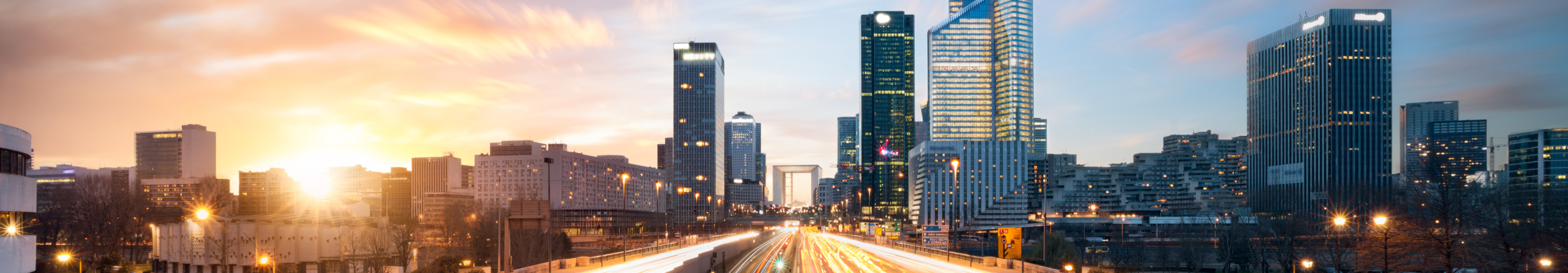 Stadtviertel La Défense in Paris mit modernen Hochhäusern und Lichtspuren des Verkehrs bei Sonnenuntergang