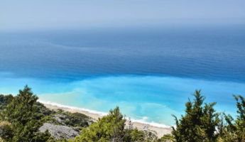 Blick auf das türkisfarbene Meer und den Strand von Samos, eingerahmt von grünen Bäumen.