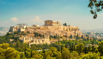 Blick auf die Akropolis in Athen, Griechenland, mit dem Parthenon-Tempel auf einem Felsen über der Stadt, umgeben von grüner Vegetation.