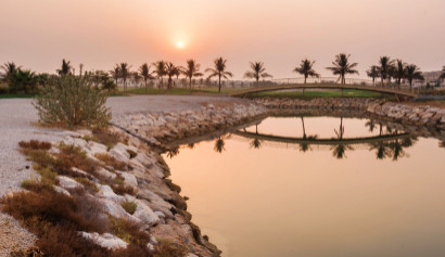 Uferdamm, Palmen, Brücke und Golfplatz mit Wohnhäusern in Ras AI Khaimah bei Sonnenuntergang