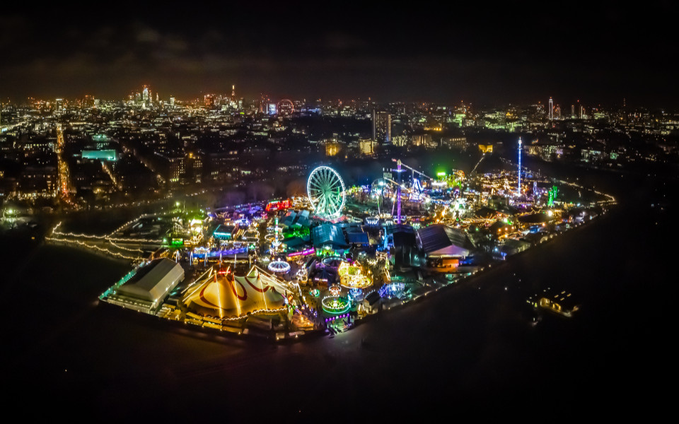 Lichtermeer des Hyde Park Winter Wonderland in London, einem der schönsten Weihnachtsmärkte weltweit, mit Riesenrad, festlich geschmückten Attraktionen und funkelnden Lichtern vor der beeindruckenden Skyline der Stadt.