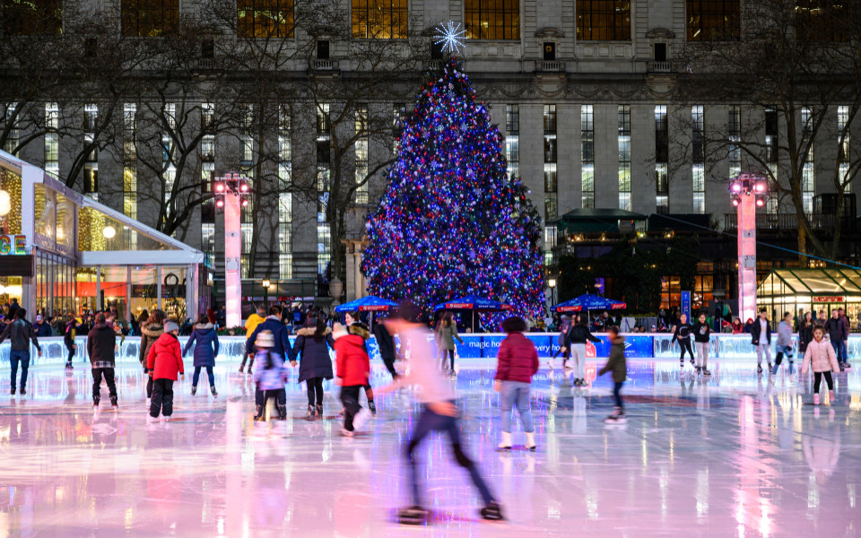 Eisbahn im Bryant Park mit funkelndem Weihnachtsbaum und fröhlichen Menschen in winterlicher Atmosphäre mitten in New York City.