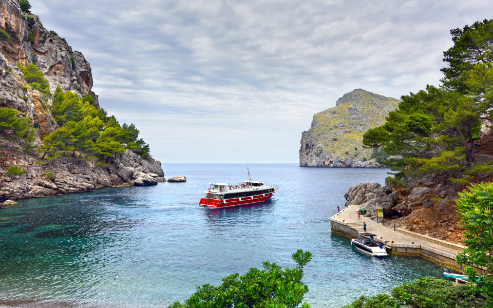  Mallorca Ausflugstipp: Malerische Bucht von Sa Calobra auf Mallorca mit kristallklarem Wasser, steilen Felswänden und einem Boot, das am Pier anlegt.	