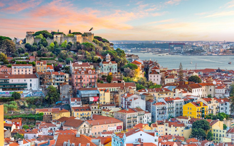 Panoramablick über Lissabon mit der beeindruckenden Burg São Jorge, farbenfrohen Häusern und dem glitzernden Tejo-Fluss im Abendlicht.