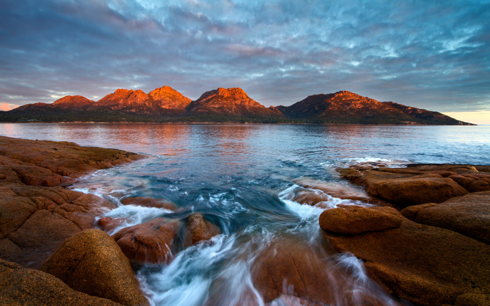 Sonnenuntergang über den Gefahren mit Alpenglühen und fließendem Wasser über Felsen, Freycinet-Nationalpark, Coles Bay, Tasmanien, Australien