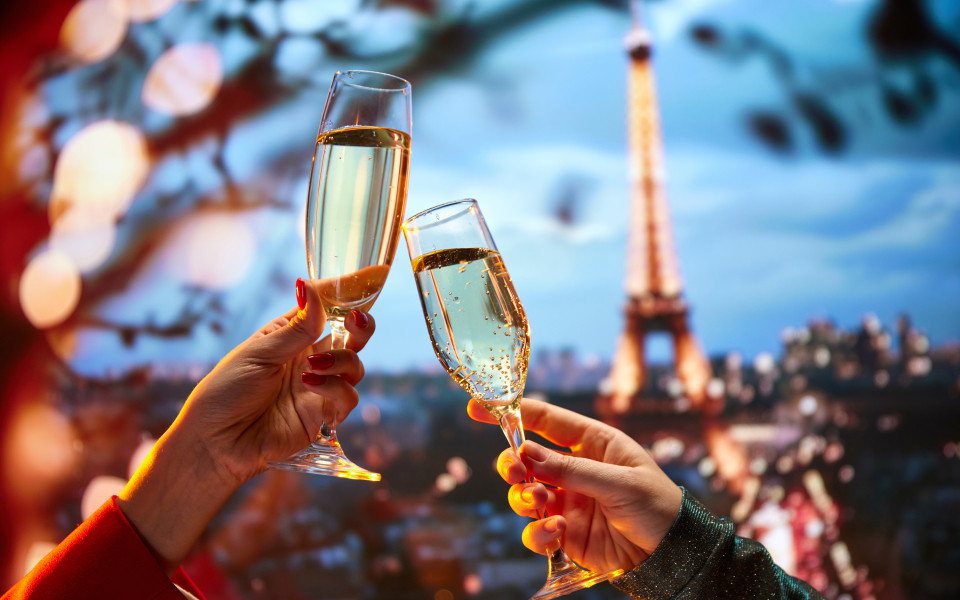 Auf der Terrasse eines feinen Restaurants in Paris mit Blick auf den Eifelturm stoßen zwei Freuen mit Champagner an