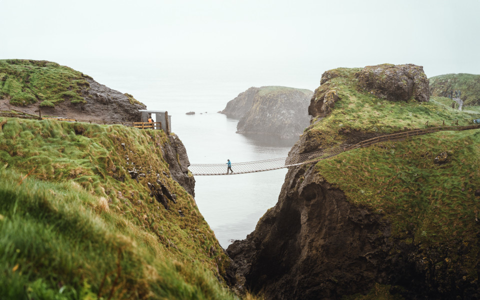 Frau in blauer Regenjacke an der Carrick-A-Rede Hängebrücke.