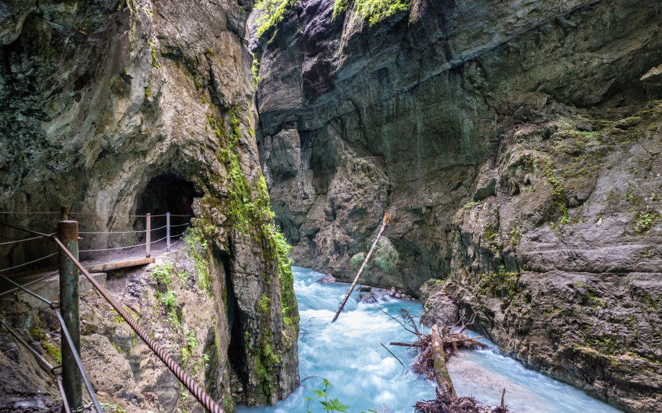 Schmale Schlucht mit türkisblauem Wildbach, steilen Felswänden und einem in den Fels gehauenen Wanderweg mit Geländer in der Partnachklamm bei Garmisch-Partenkirchen, Bayern. 